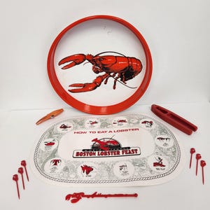 Puede incluir: Una bandeja de servir roja y blanca con temática de langosta con un gráfico de langosta. Incluye un mantel individual con instrucciones, pinchos de langosta, un rompecocos y un utensilio en forma de langosta. El mantel individual dice "HOW TO EAT A LOBSTER" y "BOSTON LOBSTER FEAST."