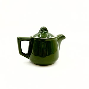 May include: A small, dark green ceramic teapot with a white lid and a white rim around the spout.