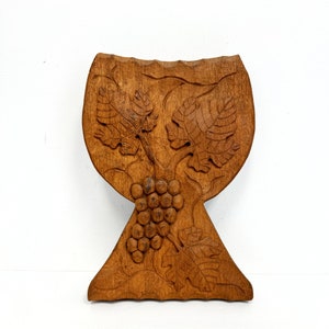 May include: A wooden wall hanging in the shape of a wine glass with a carved grapevine and grapes.