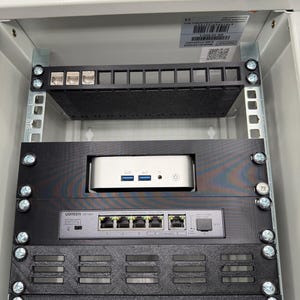 Könnte beinhalten: Ein Serverschrank mit mehreren Komponenten. Der obere Bereich hat eine schwarze Blende mit mehreren Anschlüssen. Darunter befindet sich ein silberner Computer und ein UGREEN-Netzwerk-Switch mit mehreren Anschlüssen. Das Rack ist in einem weißen Schrank montiert.