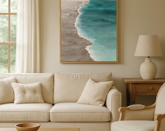 May include: An abstract framed canvas art piece depicting a coastal scene with turquoise water and a sandy shore. The artwork is displayed above a beige sofa in a living room setting. The room also features a wooden coffee table, a side chair, and a table lamp.