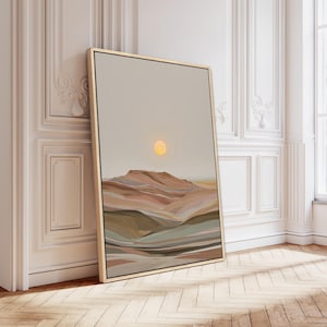 May include: A framed landscape art print featuring a desert scene with a yellow sun and layered, colorful hills. The artwork is in a gold frame and leans against a white wall with decorative molding. The color palette includes beige, brown, and muted greens.