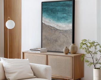 May include: A framed abstract art print depicting a coastal scene with turquoise water, white waves, and a sandy shore. The artwork is displayed above a wooden cabinet with decorative vases and a small plant. A white sofa and a modern floor lamp are also visible.