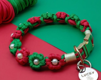 Puede incluir: Un collar de perro trenzado rojo y verde con un diseño de flores y una etiqueta plateada que dice "LUCKY" con un pequeño símbolo de flor.