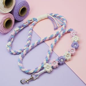 May include: A braided dog lead with a white, light purple and lavender colour scheme. The lead is decorated with small, white flowers with pearl centres. The lead has a silver clip.