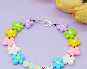 May include: A colorful bracelet featuring flower-shaped beads in various colors, including yellow, pink, green, blue, and white. The bracelet has the word "LUCKY" spelled out with letter beads. The bracelet is secured with a silver clasp.