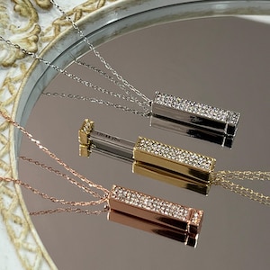 Op de afbeelding: Drie zilveren, gouden en roségouden kettingen met een rechthoekige hanger die een boodschap bevat en bedekt is met strass. De boodschap in de hanger luidt "I miss you".