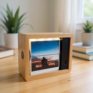 May include: A wooden photo display box with a light, natural finish. The box has a slot for displaying photos, lit by a strip of lights. The displayed photos show a couple silhouetted against a sunset. A black dial is on the side.