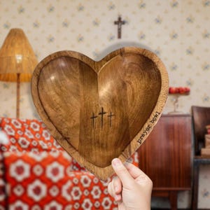 May include: A wooden heart-shaped bowl with the words "prayer bowl" engraved on the side. Three crosses are carved into the center of the bowl.
