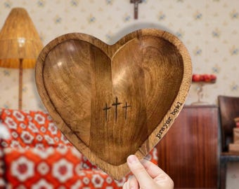 May include: A wooden heart-shaped bowl with the words "prayer bowl" engraved on the side. Three crosses are carved into the center of the bowl.