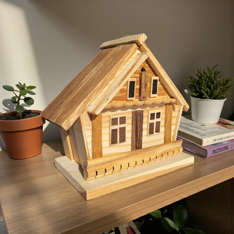 Puede incluir: Una maqueta de casa de madera hecha a mano con tejado a dos aguas, ventanas y chimenea. La casa est&aacute; hecha de tonos de madera claros y oscuros y se asienta sobre una base rectangular. El modelo se exhibe en una estanter&iacute;a de madera.