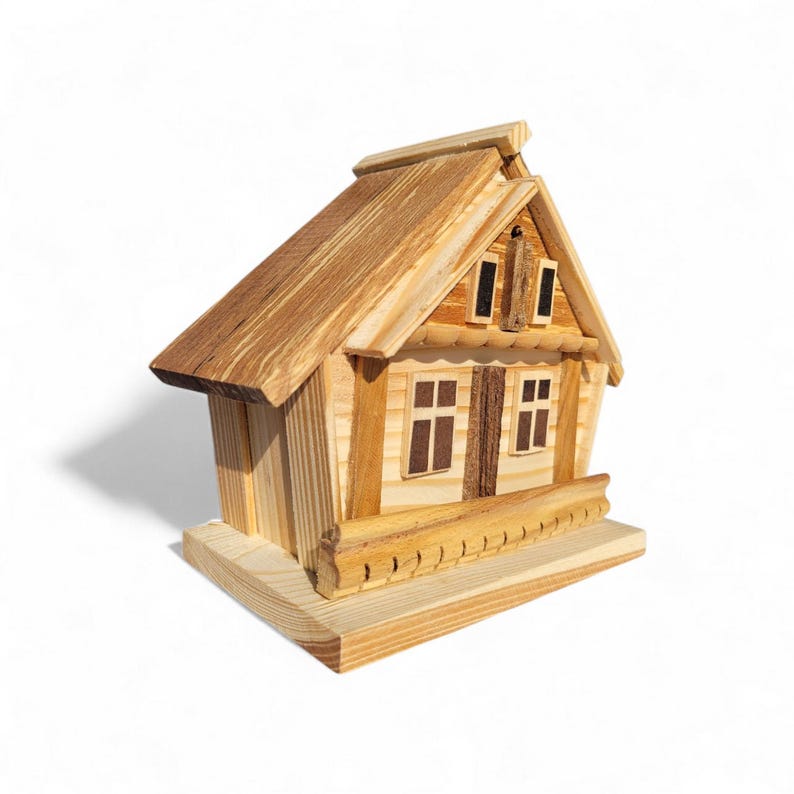 Puede incluir: Una casa de madera en miniatura con techo y paredes de color marr&oacute;n claro. La casa tiene dos ventanas, una peque&ntilde;a chimenea y una barandilla decorativa en el porche. La casa se asienta sobre una base rectangular.