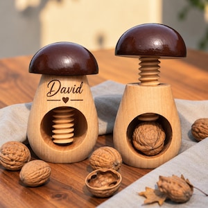 Könnte beinhalten: Zwei pilzförmige Nussknacker aus Holz mit dunkelbraunen Kappen und hellen Holzsockeln. Ein Nussknacker ist mit dem Namen David und einem Herzsymbol graviert. Beide verfügen über einen Schraubmechanismus zum Knacken von Walnüssen, die verstreut liegen.