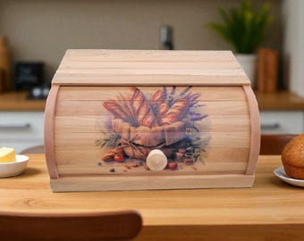 May include: Wooden bread box with a roll-top lid. The front features a painted design of bread, wheat, and lavender. The box is made of light-colored wood and sits on a wooden table. A butter dish and a muffin are also visible.