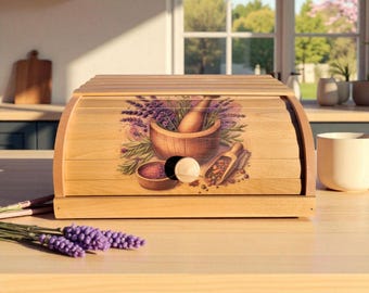May include: A light-colored wooden bread box with a roll-top lid. The front features a colorful illustration of a mortar and pestle with lavender and spices. A sprig of lavender sits in front of the box.