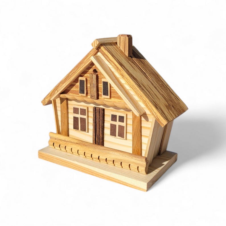 Puede incluir: Una casa de madera en miniatura con tejado a dos aguas, chimenea y peque&ntilde;as ventanas. La casa est&aacute; construida con madera clara y tiene un porche con una barandilla decorativa. El dise&ntilde;o general es r&uacute;stico y encantador.