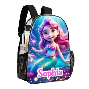 Op de afbeelding: Een transparante rugzak met een zeemeermin ontwerp. De zeemeermin heeft roze haar en een groene staart. De rugzak heeft een mesh-zak aan de zijkant en de naam "Sophia" staat op de voorkant.