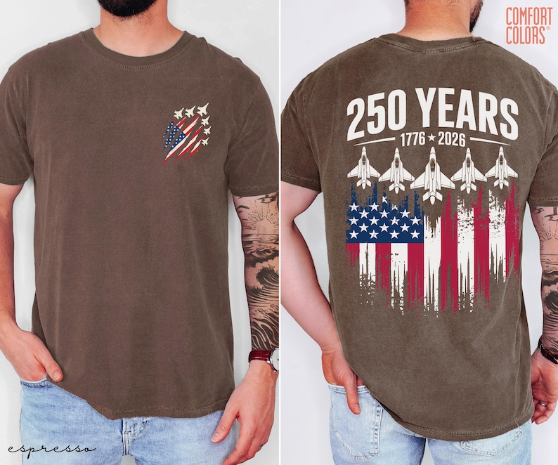 May include: A brown short-sleeve t-shirt featuring a small graphic on the front left chest of fighter jets and a distressed American flag. The back displays the text 250 YEARS 1776-2026 above five fighter jets and a large distressed American flag.