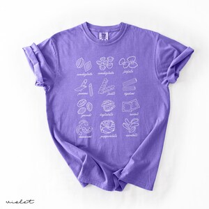 Op de afbeelding: Paars T-shirt met een witte afbeelding van verschillende soorten pasta met hun Italiaanse namen.