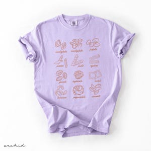 Op de afbeelding: Een lavendelkleurig T-shirt met een afbeelding van verschillende soorten pasta met hun namen onder elke afbeelding. De pastasoorten zijn:  conchiglie,  conchigliette,  farfalle,  penne,  fusilli,  spaghetti,  gnocchi,  tagliatelle,  tortellini,  macaroni,  pappardelle  en  cannelloni.
