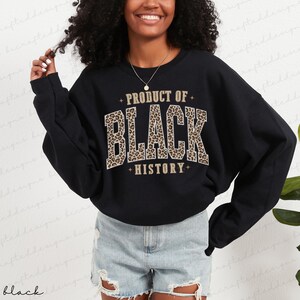 May include: Black sweatshirt with the text "PRODUCT OF BLACK HISTORY" in a leopard print design. The sweatshirt is a crew neck style and has long sleeves. The text is in a bold, collegiate-style font.