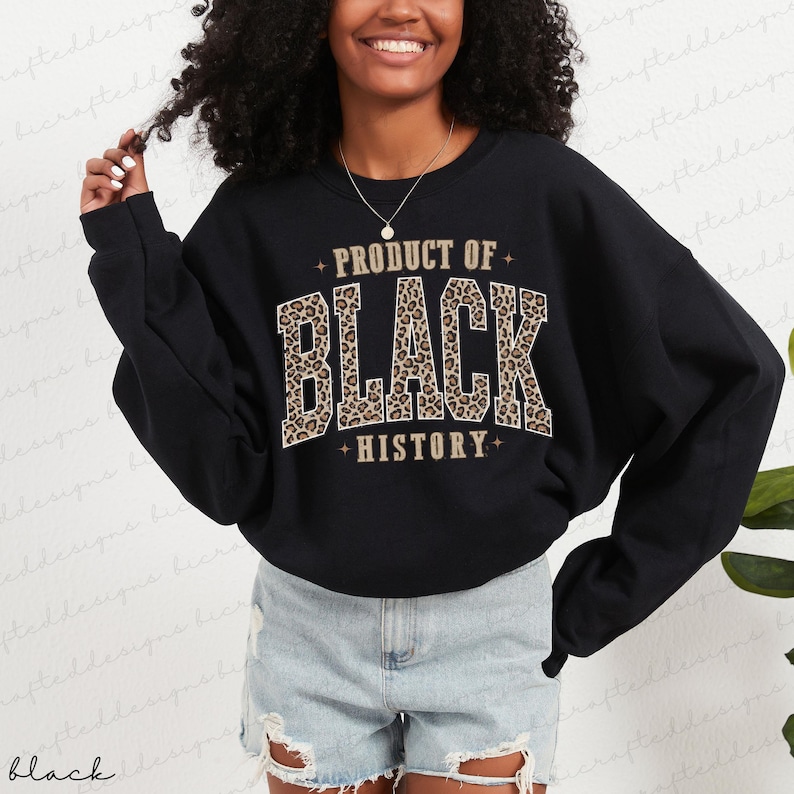 May include: Black sweatshirt with the text "PRODUCT OF BLACK HISTORY" in a leopard print design. The sweatshirt is a crew neck style and has long sleeves. The text is in a bold, collegiate-style font.