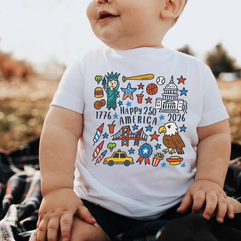 K&ouml;nnte beinhalten: Wei&szlig;es T-Shirt mit einem farbenfrohen Grafikdesign, das den Text "Happy 250 America 2026" und Illustrationen der Freiheitsstatue, eines Baseballschl&auml;gers und eines Adlers enth&auml;lt. Das Design zeigt auch Sterne und andere patriotische Symbole. F&uuml;r Kinder.