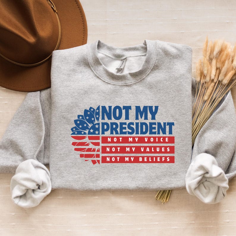 May include: Gray sweatshirt with a sunflower design and the text "Not My President" with the words "Not My Voice", "Not My Values", and "Not My Beliefs" underneath.