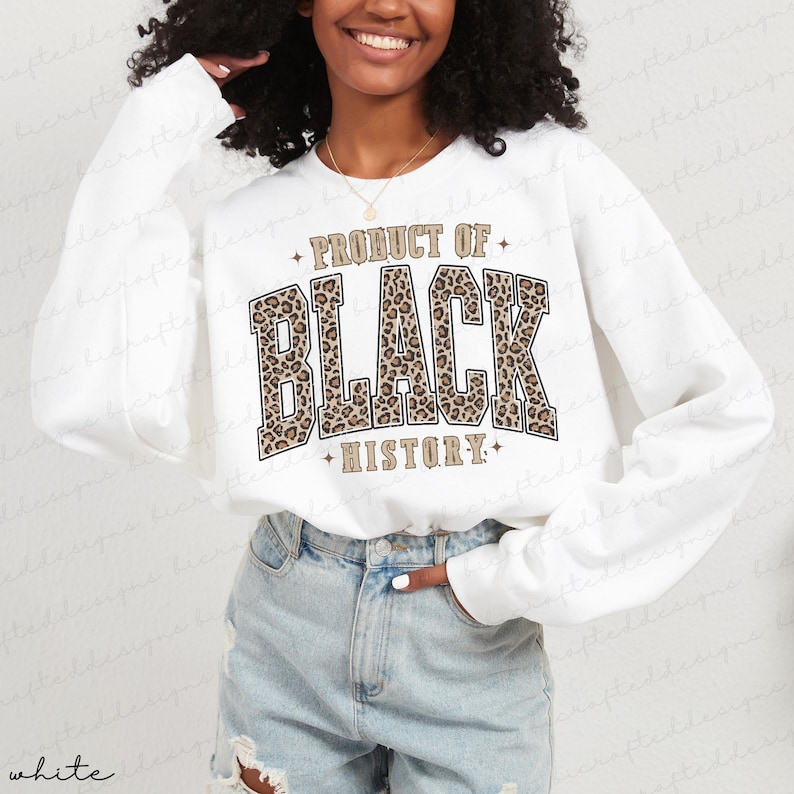 May include: White sweatshirt with long sleeves featuring the text "PRODUCT OF BLACK HISTORY" in a bold, leopard print design. The sweatshirt has a crew neck and a relaxed fit, suitable for casual wear.
