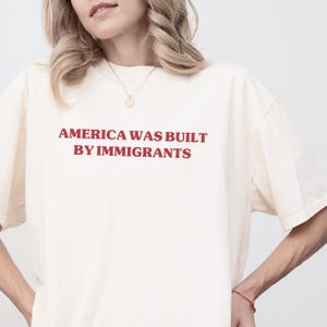 May include: A white t-shirt with the text "America was built by immigrants" printed in red.