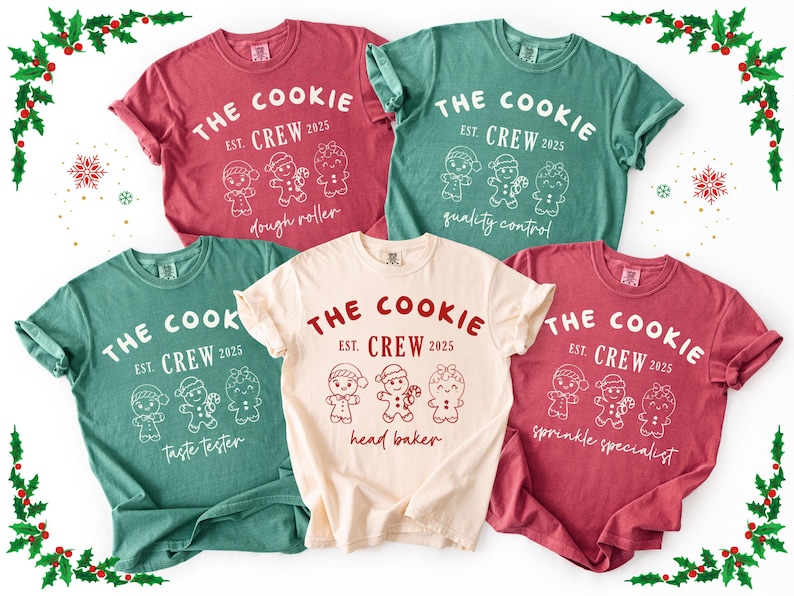 May include: A collection of five t-shirts in various colors, including red, green, and cream. Each shirt features the text "THE COOKIE CREW EST. 2025" with different gingerbread character designs and job titles like "dough roller" and "head baker."