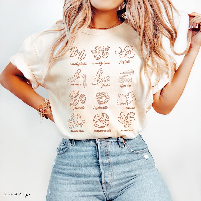 Op de afbeelding: Een wit T-shirt met bruine contouren van verschillende soorten pasta, waaronder conchiglie, farfalle, penne, fusilli, rigatoni, gnocchi, tagliatelle, ravioli, macaroni, pappardelle en cavatelli.