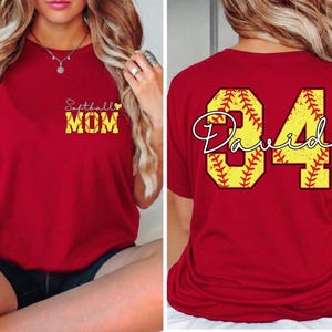 Puede incluir: Camiseta roja con "Softball MOM" en amarillo y blanco en la parte delantera. La parte trasera presenta un dise&ntilde;o de b&eacute;isbol amarillo con el nombre "David" y el n&uacute;mero "84".