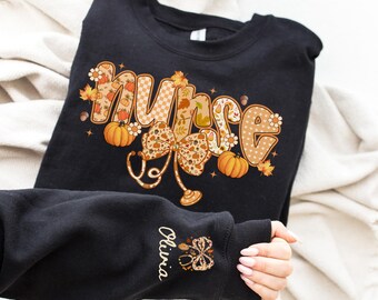 May include: Black sweatshirt with the word "Nurse" in a fall-themed design. The word is decorated with pumpkins, leaves, and a bow with a stethoscope. The sleeve has the name "Olivia" and a matching design.