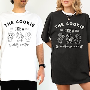 May include: Two t-shirts, one white and one black, featuring the text "THE COOKIE CREW EST. 2025" above three gingerbread people illustrations. The white shirt says "quality control" below the illustrations, while the black shirt says "sprinkle specialist".