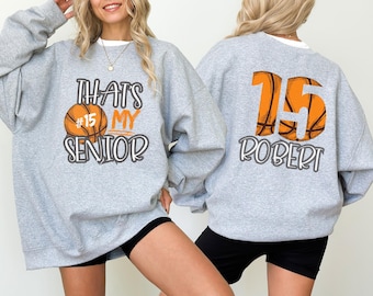 May include: Two grey sweatshirts with basketball graphics. One sweatshirt says "That's My Senior" with a basketball and the number 15. The other sweatshirt has a basketball with the number 15 and the name "Robert".