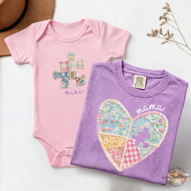 May include: A light pink ribbed baby bodysuit featuring a floral and plaid puzzle piece graphic with the text mini, and a purple t-shirt featuring a floral and plaid heart graphic with a puzzle piece cutout and the text mama.