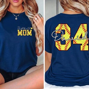 Puede incluir: Camiseta azul marino con "Softball MOM" en letras amarillas y negras en la parte delantera. La parte trasera de la camiseta presenta un gran dise&ntilde;o de b&eacute;isbol amarillo y rojo con el nombre "David" y el n&uacute;mero "84".