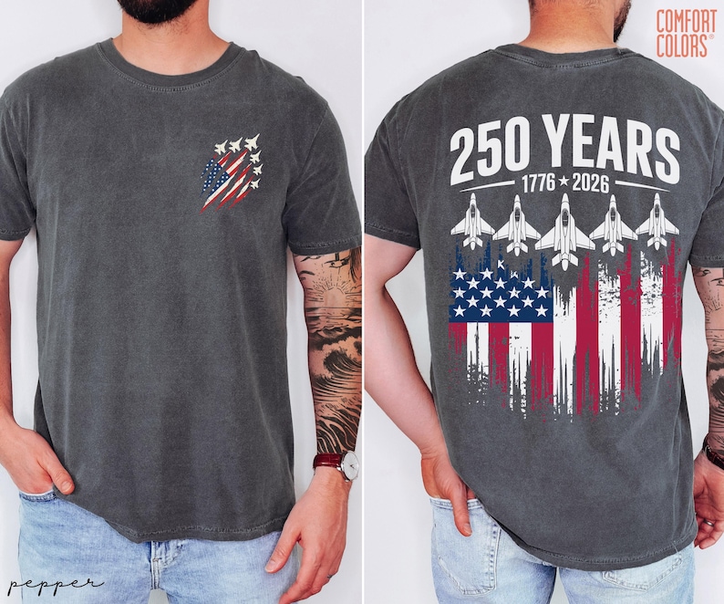 May include: A charcoal gray short-sleeve t-shirt featuring a small graphic on the front left chest of a stylized American flag with fighter jets. The back displays the text 250 YEARS 1776-2026 above five fighter jets and a distressed American flag.