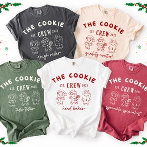 May include: Five t-shirts in various colors, each featuring the text "THE COOKIE CREW EST. 2025" with gingerbread person illustrations. The roles listed are dough roller, quality control, taste tester, head baker, and sprinkle specialist.