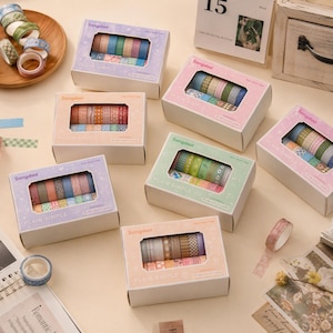 May include: Several rectangular cardboard boxes labelled Songdao Plain Simple, each containing multiple rolls of patterned washi tape. The boxes feature clear windows displaying various colourful designs, including stripes, dots, and floral patterns.