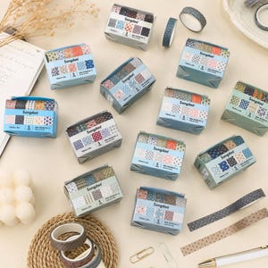 May include: Multiple Songdao brand washi tape sets in rectangular boxes, each containing five rolls with various geometric and floral patterns. The sets feature blue, pink, brown, and green color palettes, with individual rolls displayed nearby.