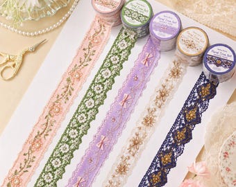 Puede incluir: Un juego de cinco rollos de cinta Floral Trim Series Tape en rosa, verde, lavanda, beige y azul marino. Cada rollo presenta intrincados patrones de encaje con motivos florales, pequeños lazos y detalles de cuentas sobre una superficie blanca.