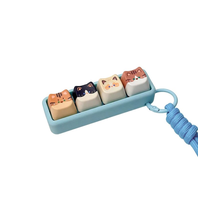 Peut inclure: Un ensemble de quatre touches de clavier sur le th&egrave;me des chats dans un plateau bleu clair avec une lani&egrave;re assortie. Chaque touche pr&eacute;sente un motif de visage de chat diff&eacute;rent dans des tons orange, noir et blanc. Les touches sont carr&eacute;es et ont une finition lisse.