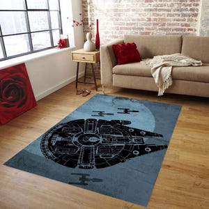 May include: A rectangular blue rug with a black spaceship design and a moon backdrop. The rug is placed on a wooden floor in a living room. The rug is a Star Wars themed product, suitable for a living room or bedroom.