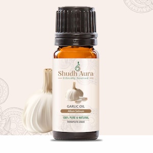 Puede incluir: Una botella de vidrio marrón de aceite esencial de ajo con una tapa negra. La etiqueta de la botella es blanca con texto verde que dice "Shudh Aura Ethically Sourced Garlic Oil Allium Sativum 100% Pure & Natural Therapeutic Grade". Un bulbo de ajo entero es visible en el fondo.