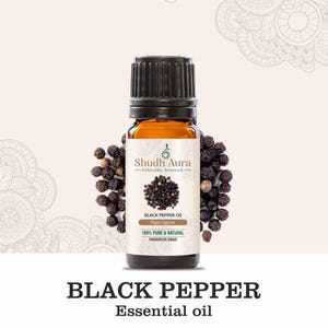 May include: A small amber glass bottle with a black cap containing black pepper essential oil. The bottle is labeled "Shudh Aura Ethically Sourced Black Pepper Oil Piper nigrum 100% Pure & Natural Therapeutic Grade". Black peppercorns are scattered around the bottle.