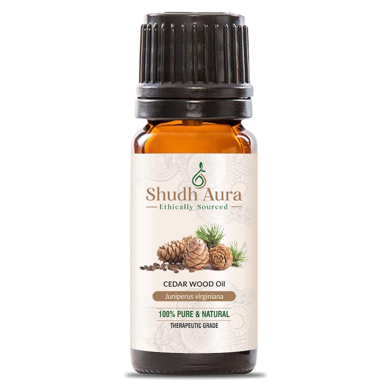 May include: A brown glass bottle of Cedar Wood Oil with a black cap. The label features the text "Shudh Aura - Ethically Sourced" and "CEDAR WOOD OIL Juniperus virginiana". The label also states "100% PURE & NATURAL THERAPEUTIC GRADE".