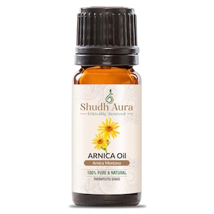 May include: A brown glass bottle with a black cap, labeled "Shudh Aura Ethically Sourced ARNICA Oil Arnica Montana 100% PURE & NATURAL THERAPEUTIC GRADE". The label features a yellow flower with green leaves.