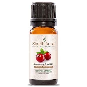 May include: A brown glass bottle of cranberry seed oil with a black cap. The label features the text "Shudh Aura" and "Cranberry Seed Oil." Two red cranberries and green leaves are also shown. The label states the oil is 100% pure and natural.